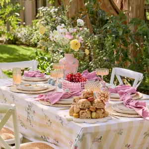 Outdoor Easter table setting with striped white and yellow table cloth, pink napkins and beige dinnerware
