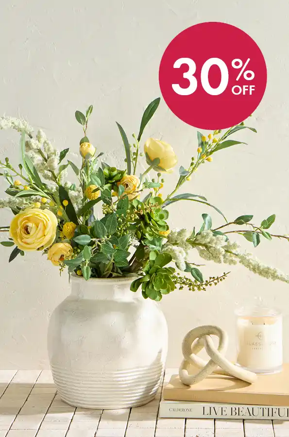 Large off white vase with yellow flower arrangement next to a candle and decor pieces.